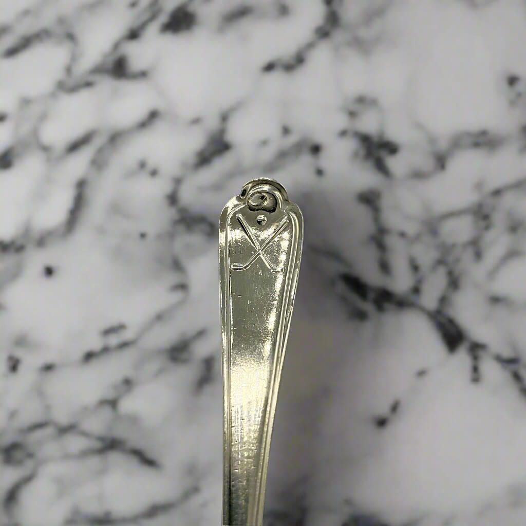 Silver spoon handle showing a goldf motif with a marble worktop background 