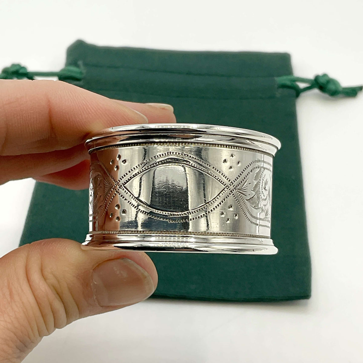 Antique silver napkin ring held in a hand with a green gift bag and white background 