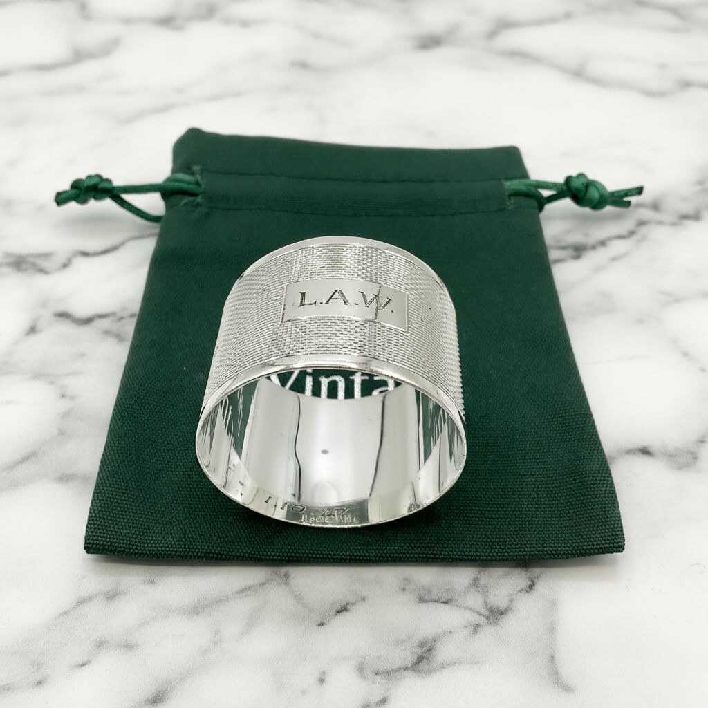 Silver napkin ring with LAW ngraved on the front on a green gift bag and marble background 