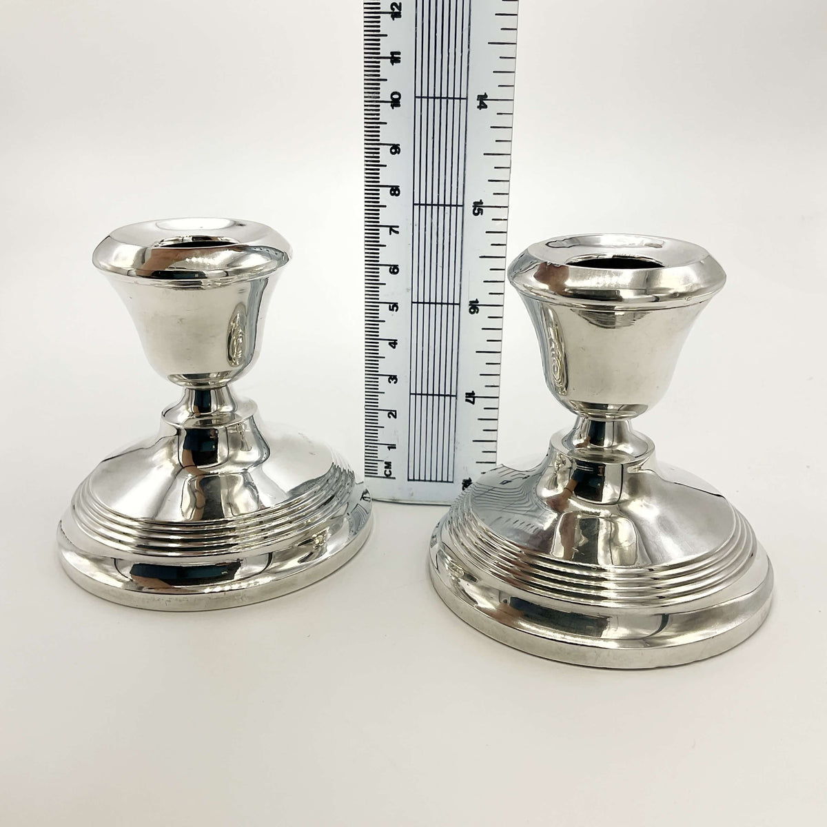 Two silver candle holders with a ruler between them showing their height as 8cm with a white background