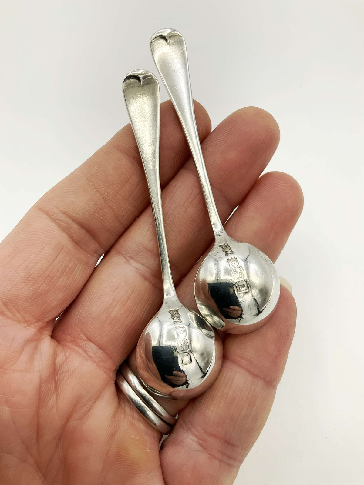Two silver spoons held in a hand against a white background