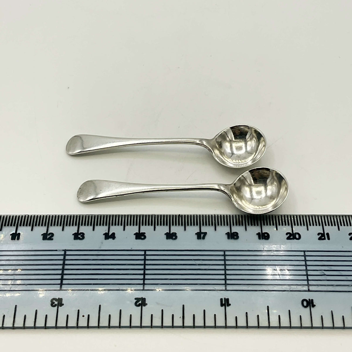Two silver spoons next to a ruler on a white background