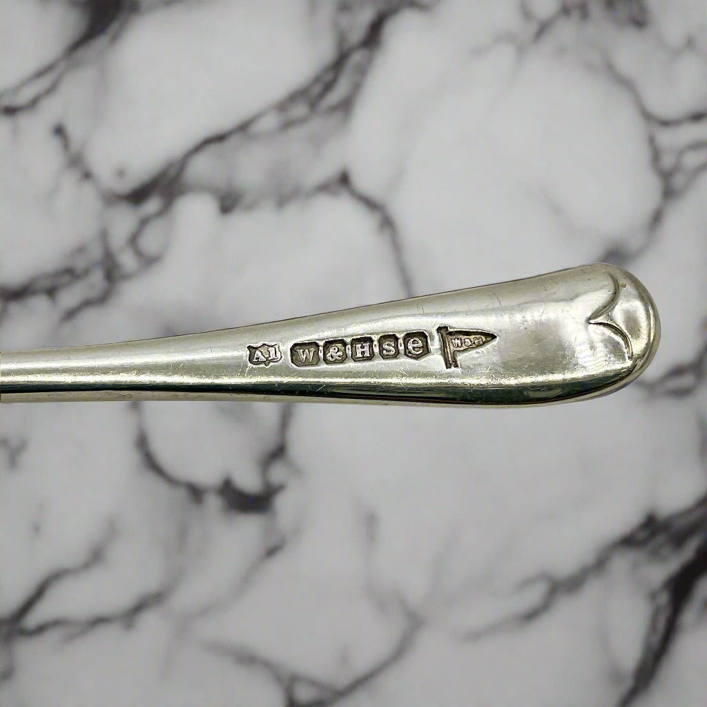 Silver spoon handle with Walker and Hall maker’s mark on a marble background