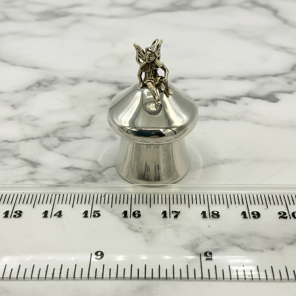 Silver pill box on a marble surface with a ruler for scale.