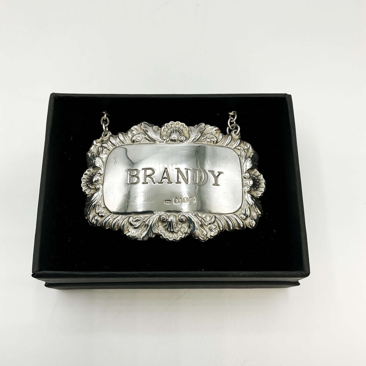 Decorative silver brandy decanter label on a black box with 'BRANDY' engraved on a white background 