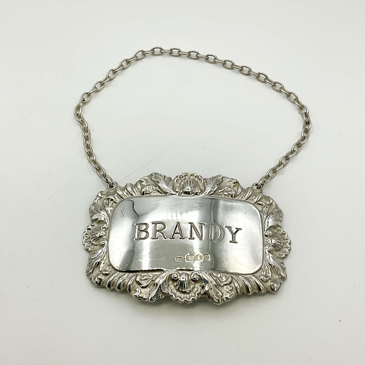 Silver brandy decanter label with ornate design on a white background
