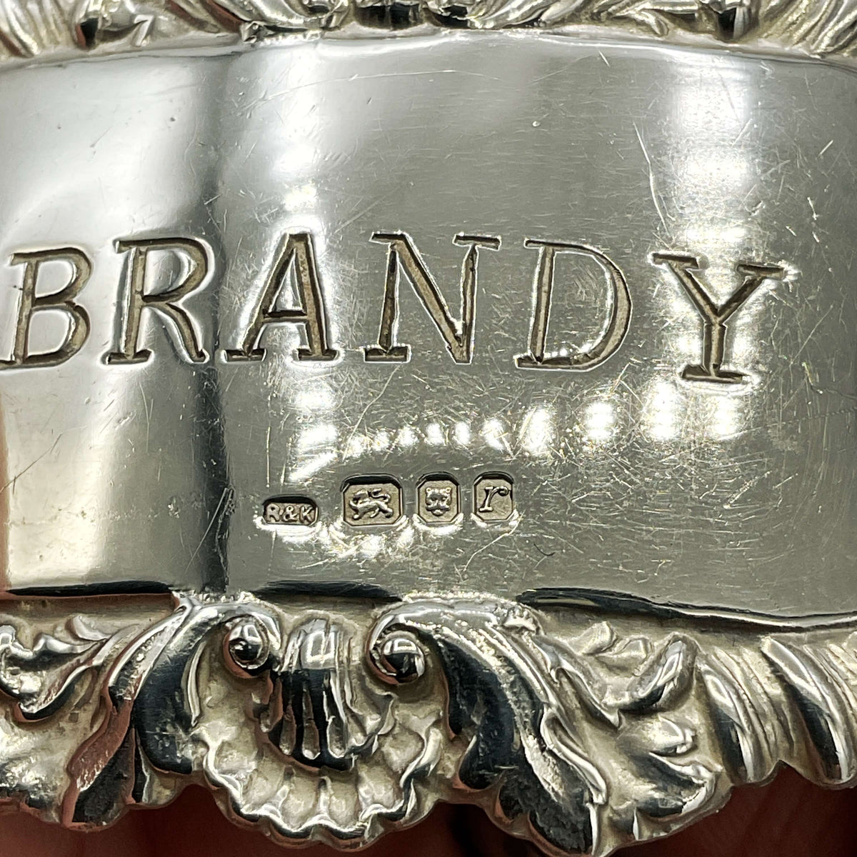 Silver brandy decanter label with 'BRANDY' engraving and decorative top showing hallmarks.