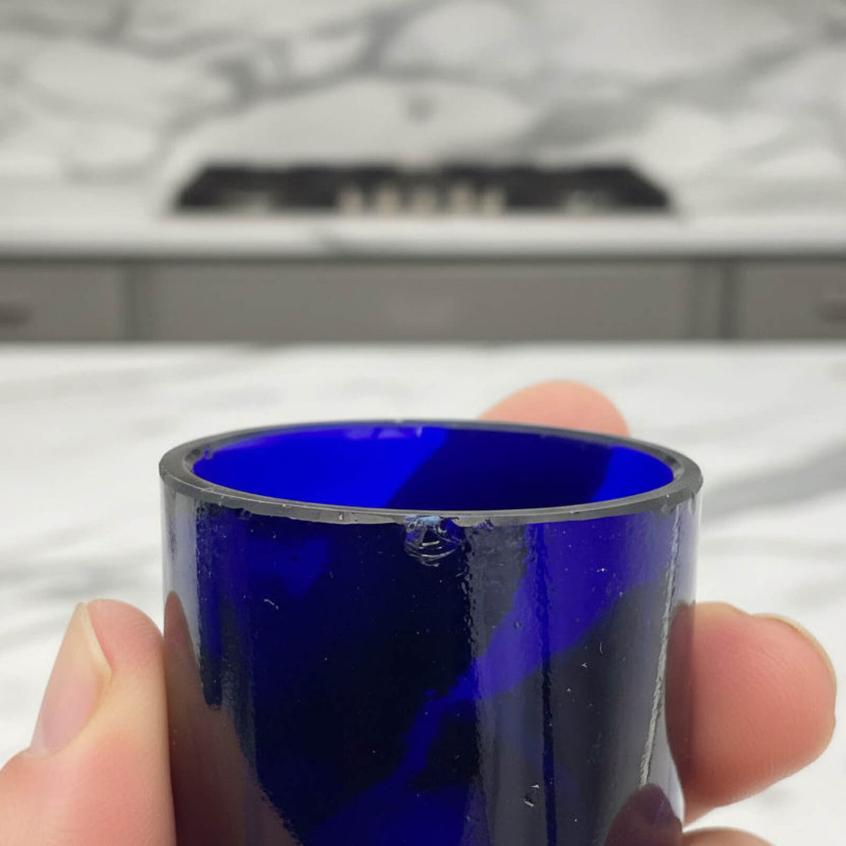 Hand holding a blue glass liner with a kitchen in the background