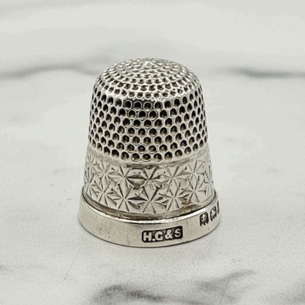 Silver thimble with intricate design on a marble background