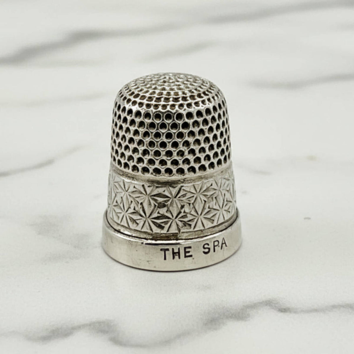 Silver thimble with intricate patterns on a marble surface