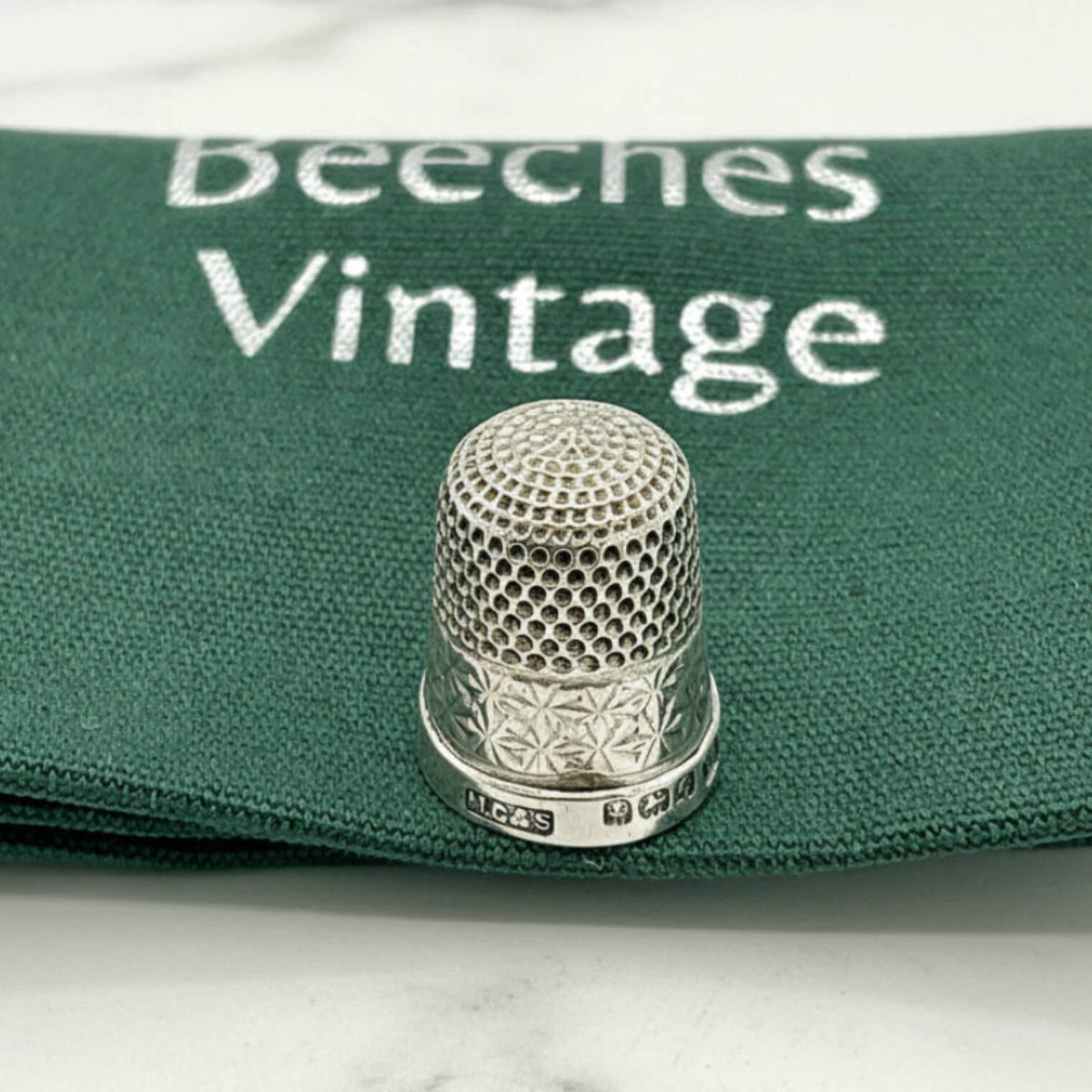 Silver thimble on a green fabric with 'Beeches Vintage' branding