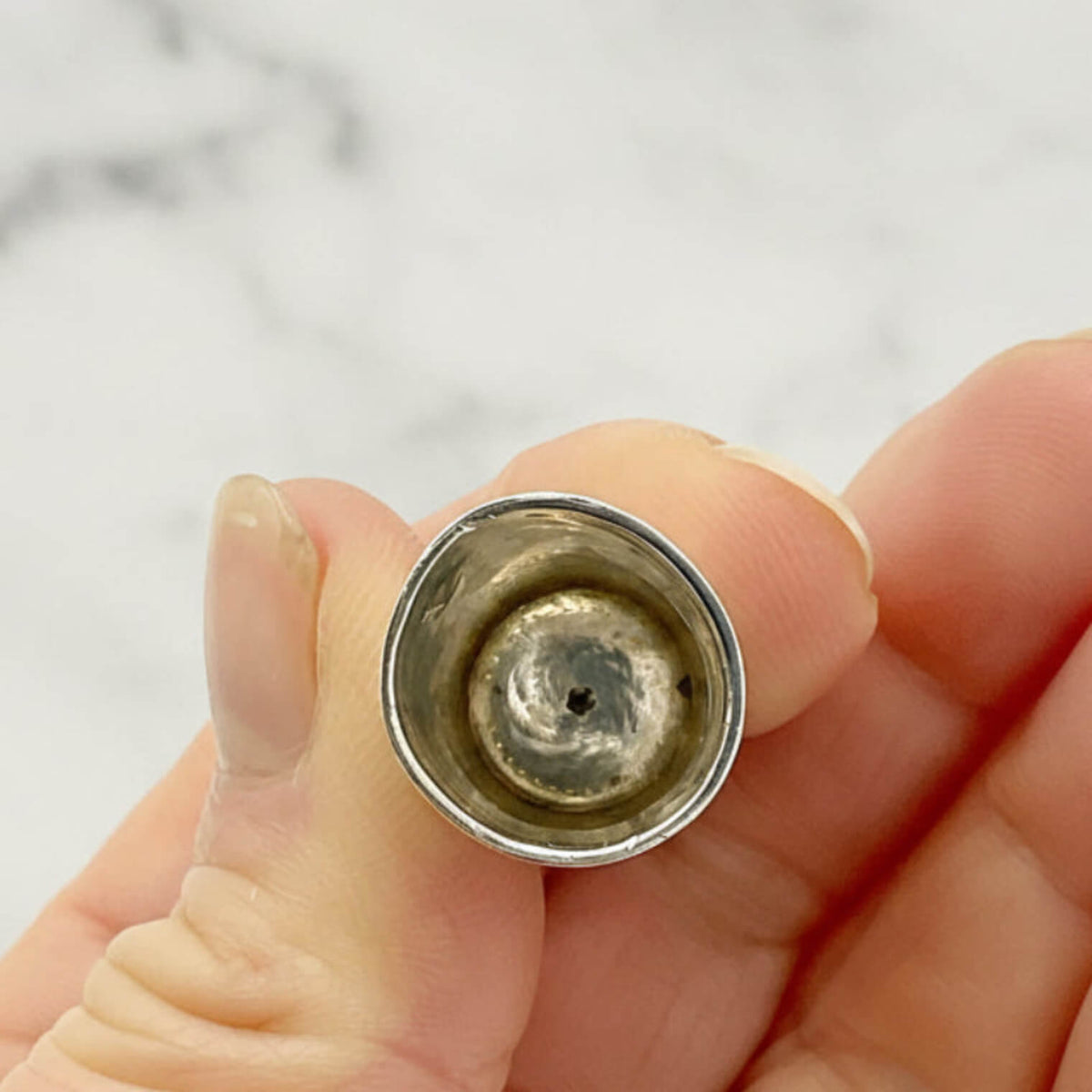 Inside of silver thimble held between fingers against a neutral background