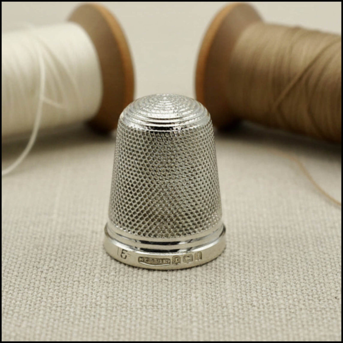 Silver thimble on a fabric surface with spools of thread in the background