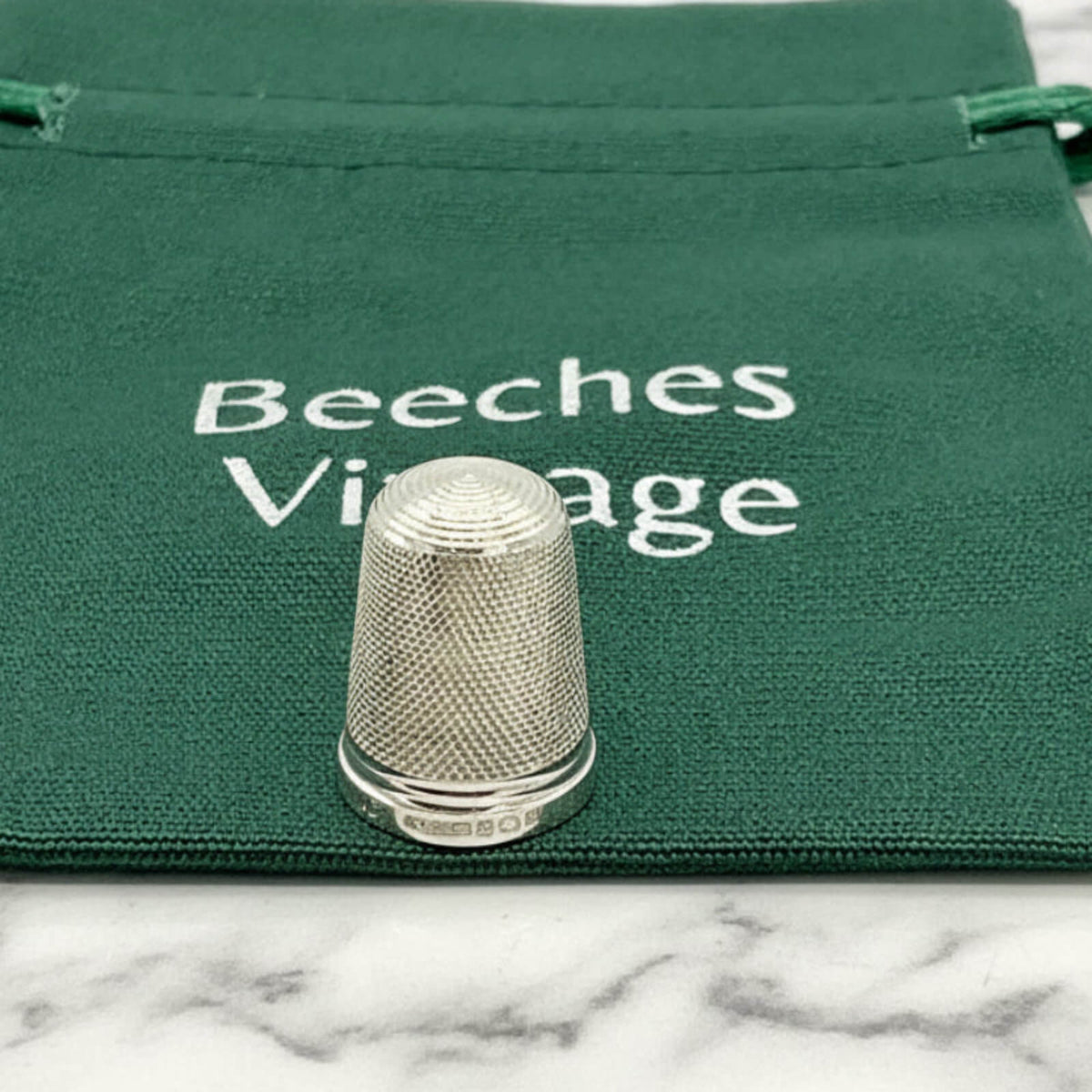 Silver thimble on a green fabric bag with 'Beeches Vintage' text.