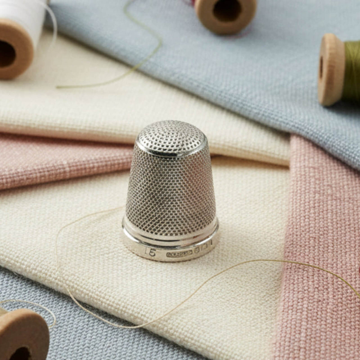 Silver thimble on a fabric background with spools of thread