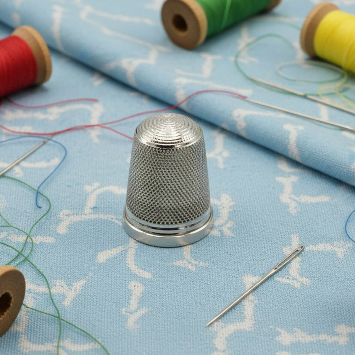 Silver thimble on a piece of fabric with spools of thread in the background