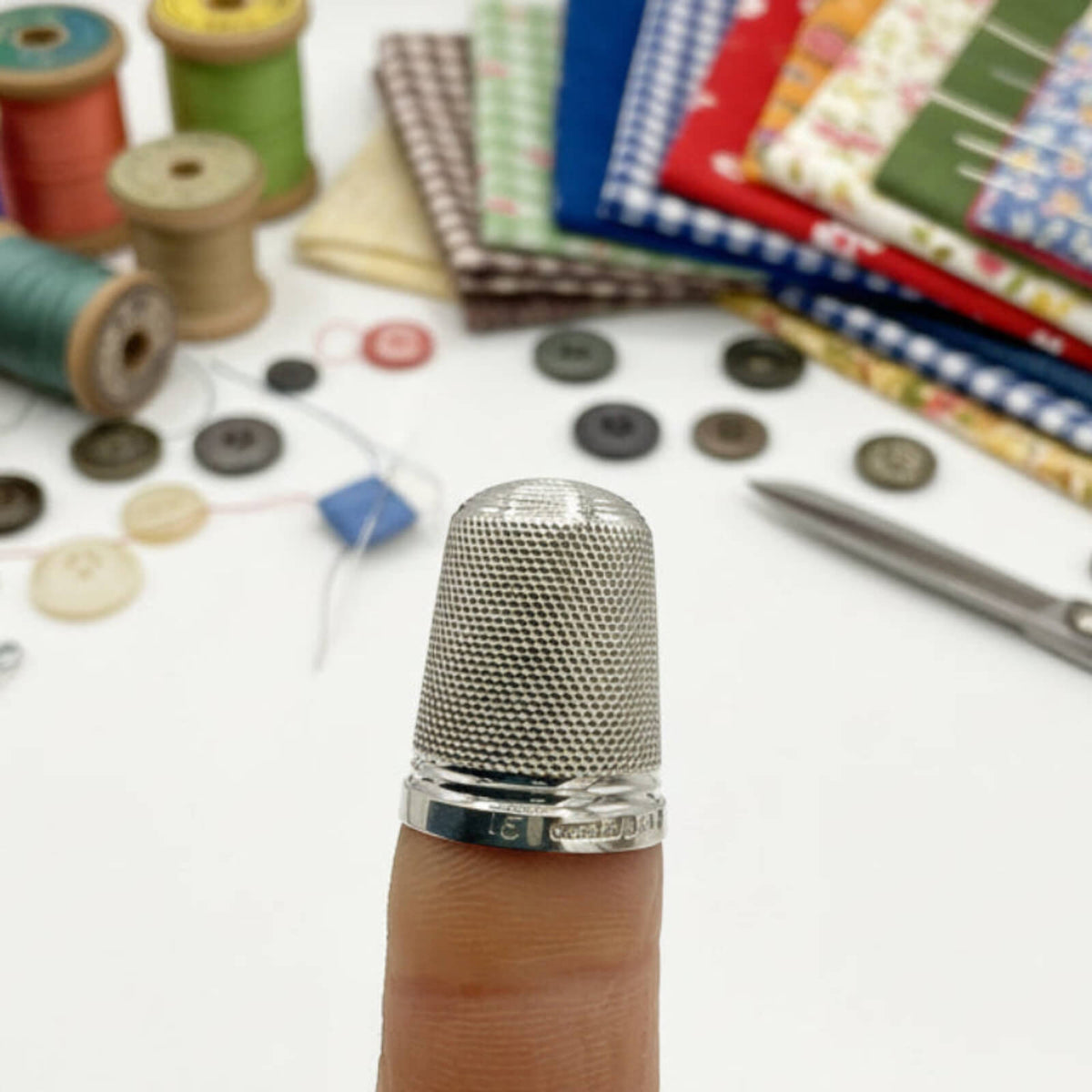 Thimble on a finger with sewing materials in the background