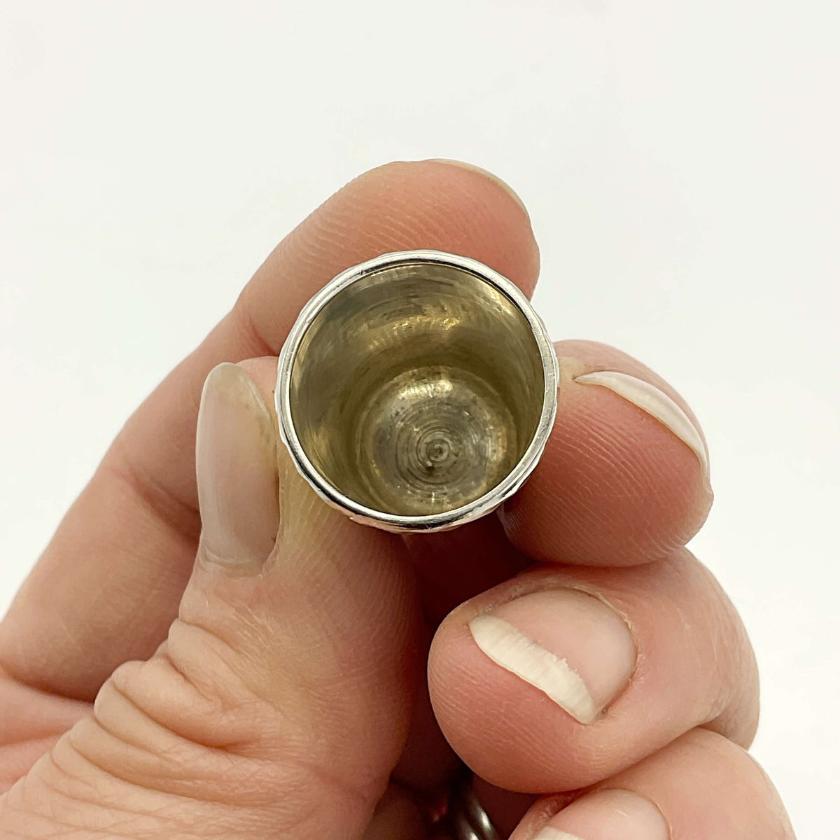 Hand holding a thimble showing the inside against a white background