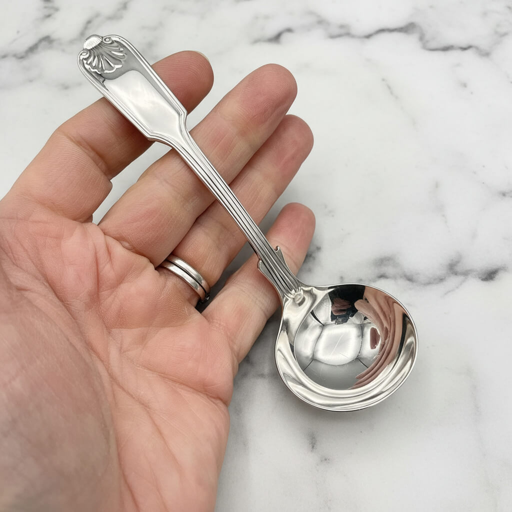 Silver plated ladle hled in a hand on a marble surface