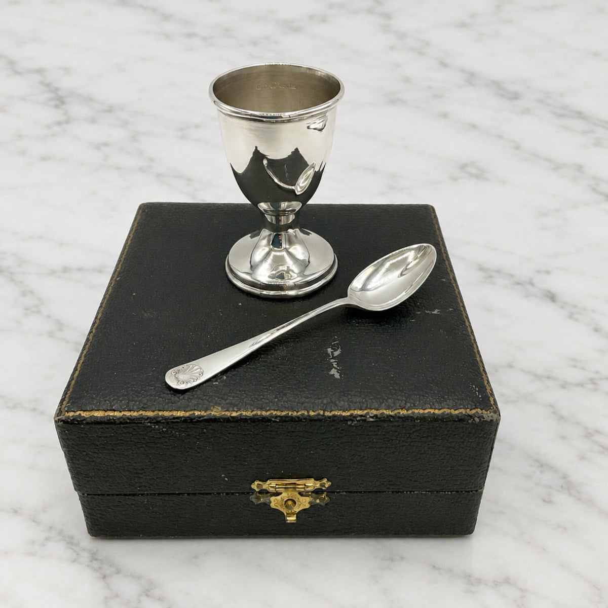 Sterling Silver Egg Cup and Spoon on top of it's origial black presentation box on a marble surface