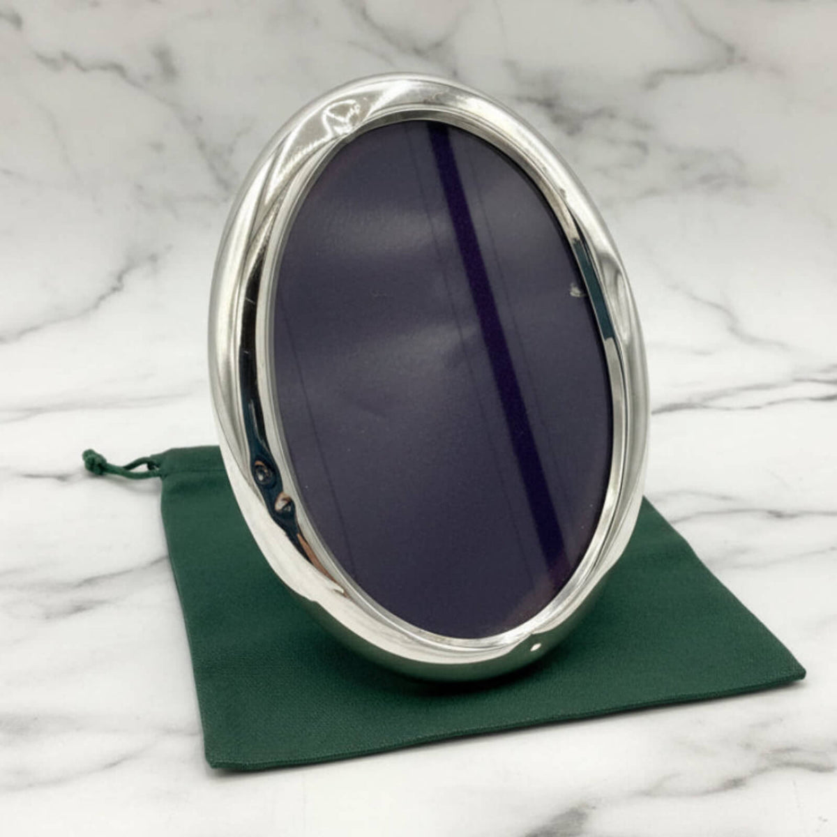 Silver oval photo frame on a green cloth with a marble background