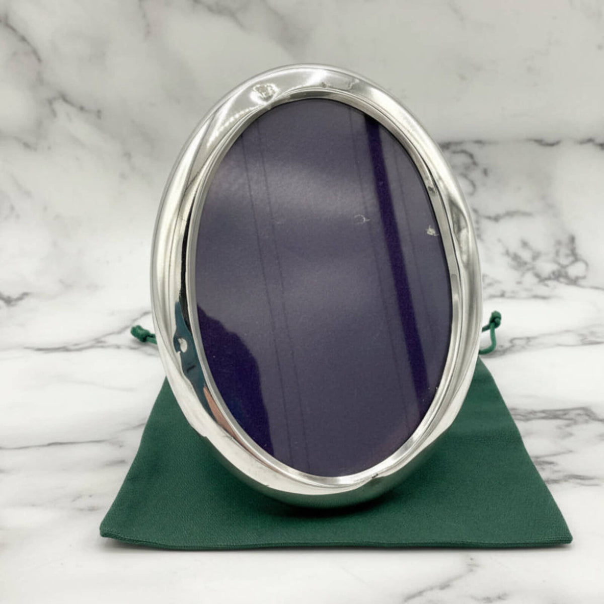 Silver oval photo frame on a green bag with a marble background