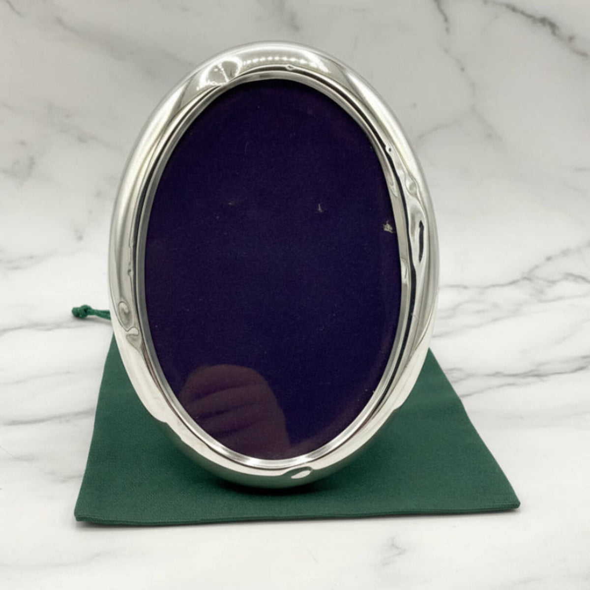 Silver oval photo frame on a green bag with a marble background