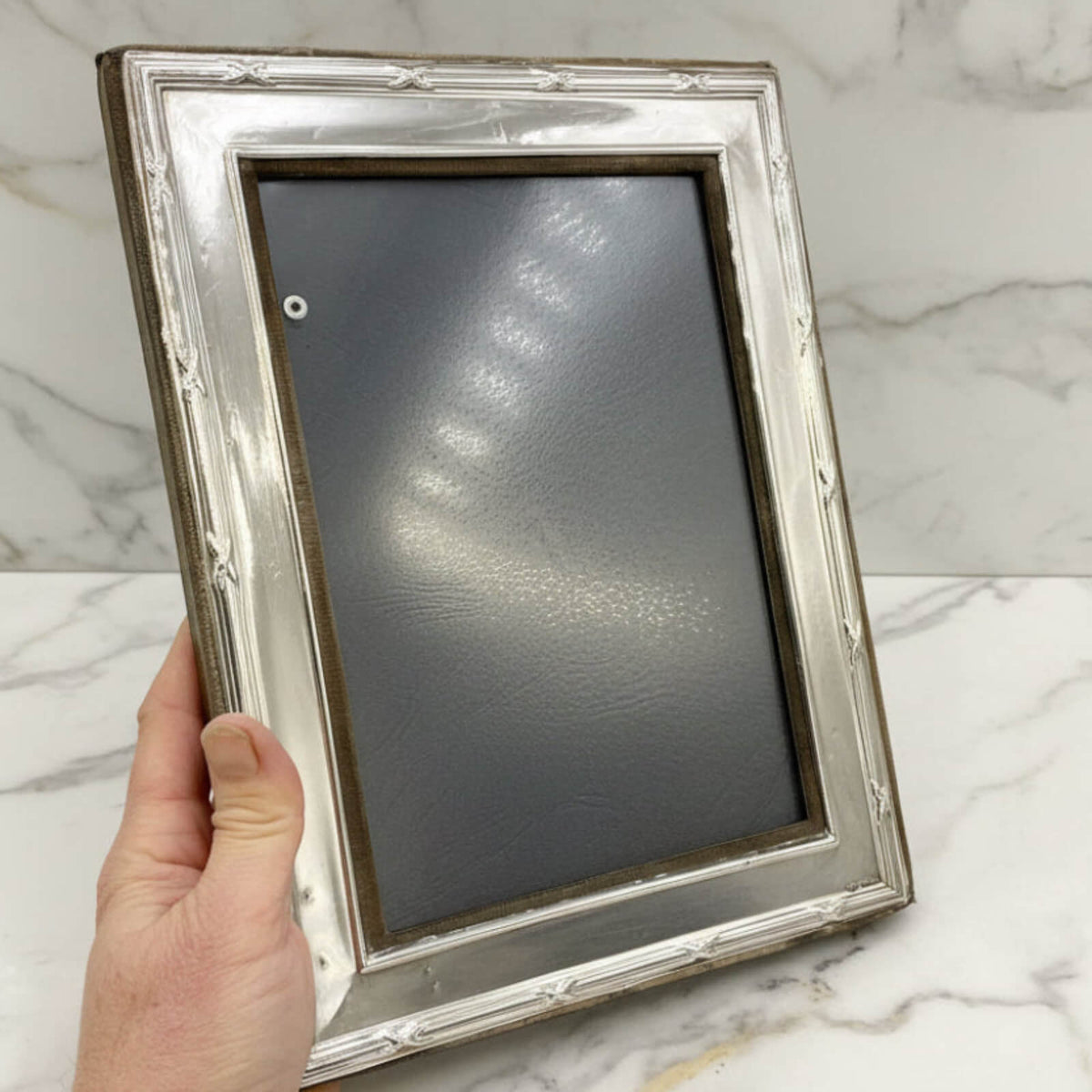Hand holding a silver picture frame against a marble background