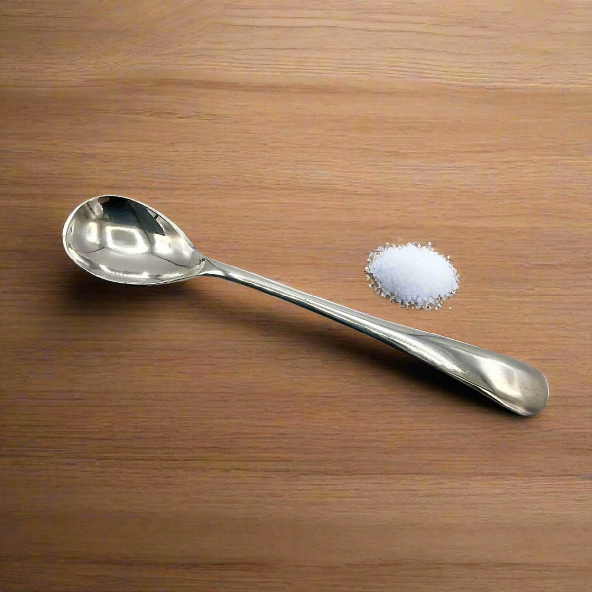 Silver spoon next to a small pile of salt on a wooden surface