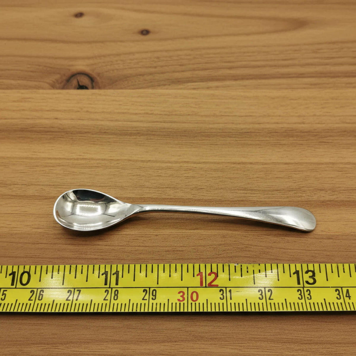 Silver spoon on a wooden surface with a yellow measuring tape for scale.