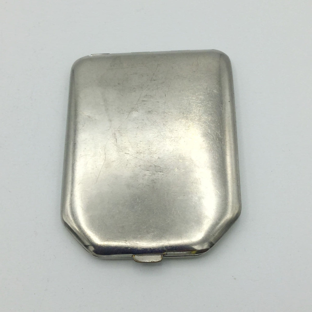 A vintage silver-toned metal powder compact with a rounded rectangular shape and a small hinge at the bottom, shown on a plain light background.