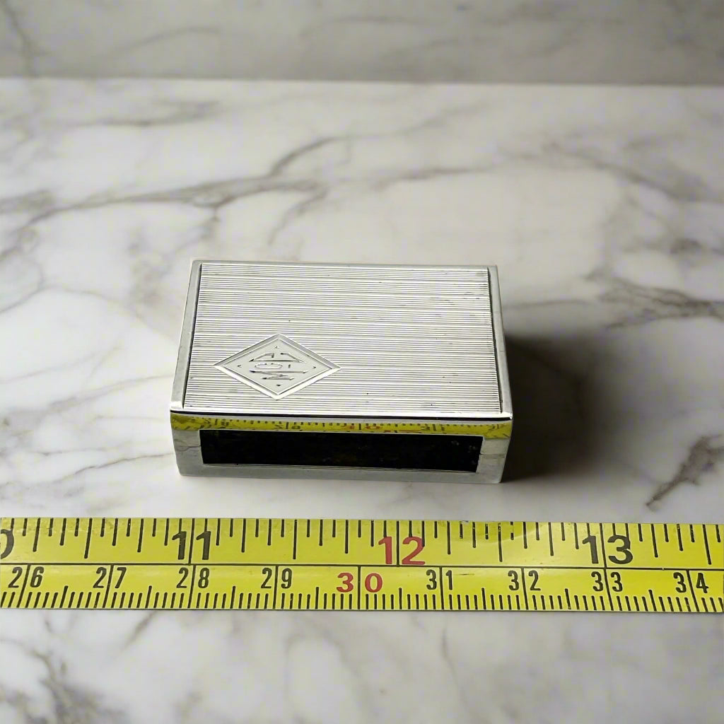 Matchbox next to tape measure on marble surface