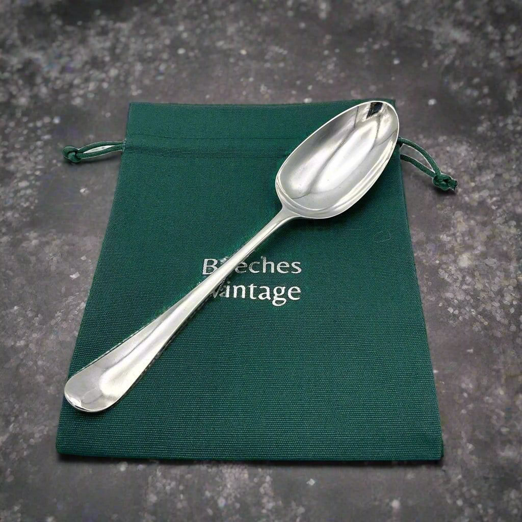 Antique silver serving spoon on a green cotton bag on a granite surface