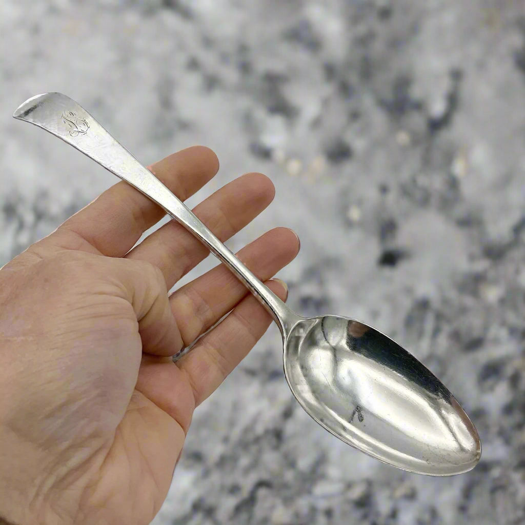 Antique silver serving spoonon held in a hand on a granite background