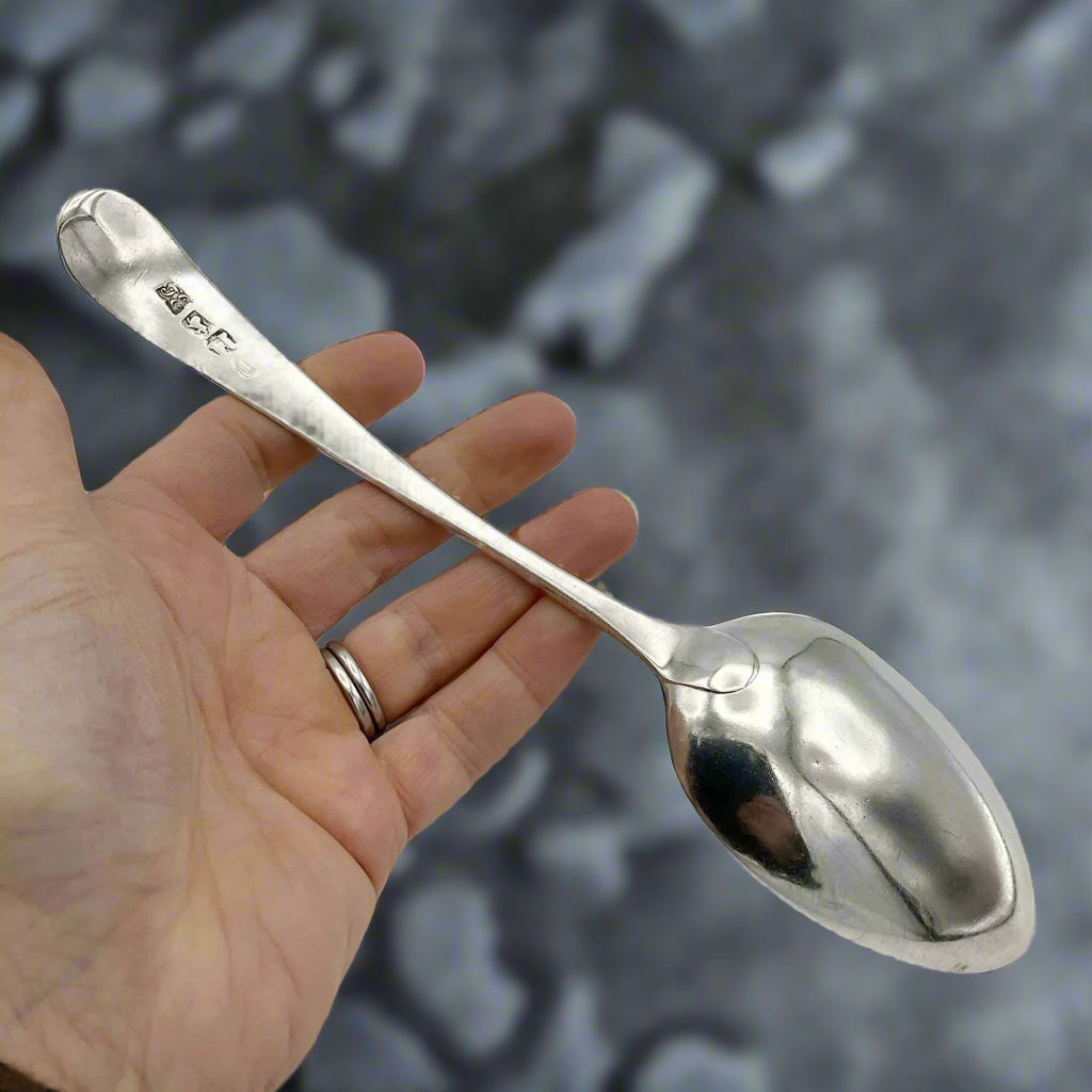 back of a Antique silver serving spoon held in a hand on a granite background