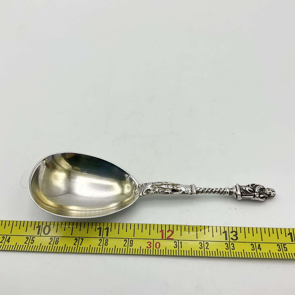 silver tea caddy spoon next to a tape measure to show ength on a white background.