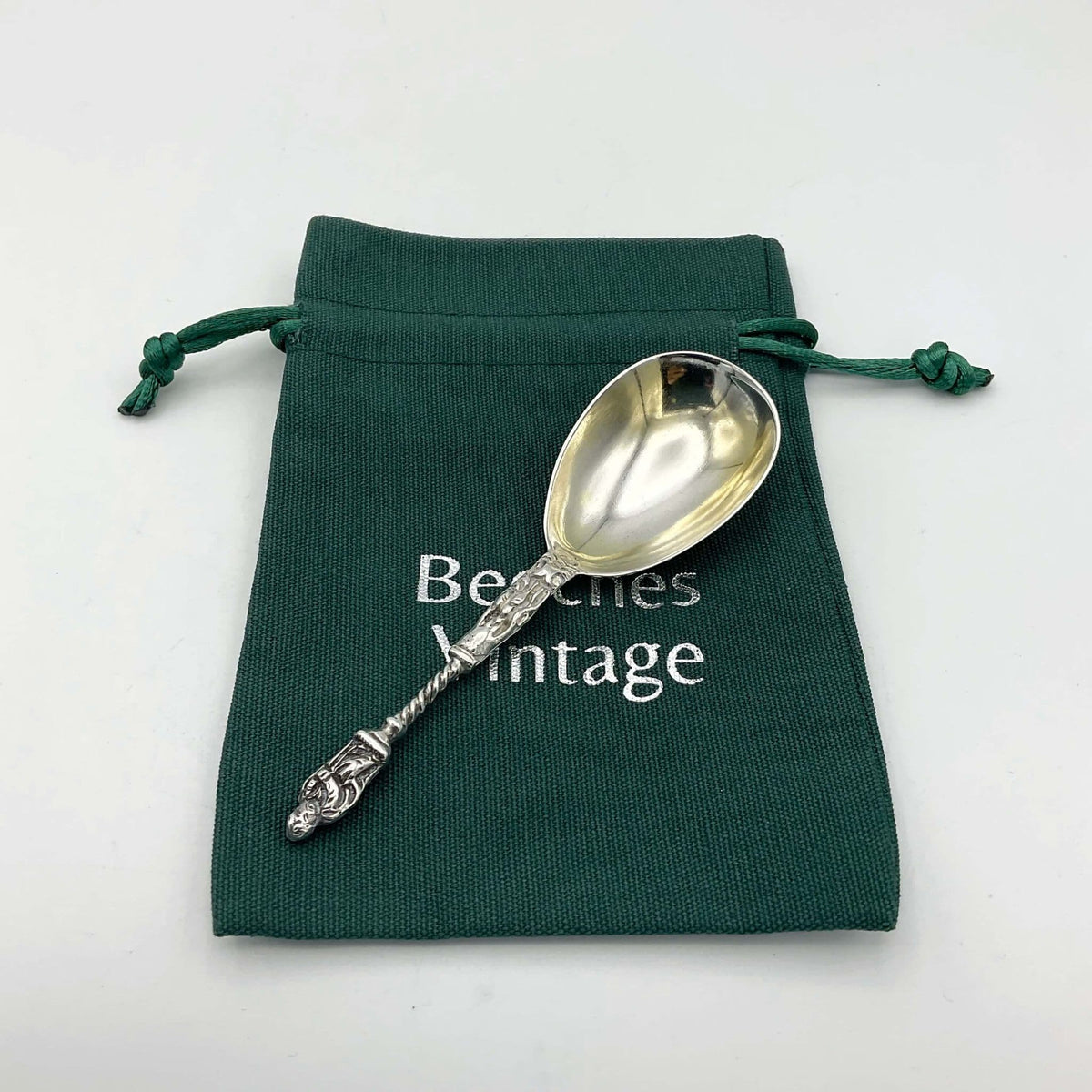 silver tea caddy spoon with an apostle handle on a green Beeches Vintage gift bag on a white background