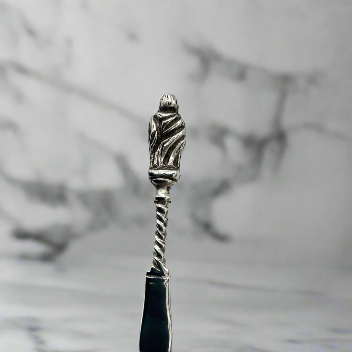 Silver-handled spoon with apostle handle on a marble background