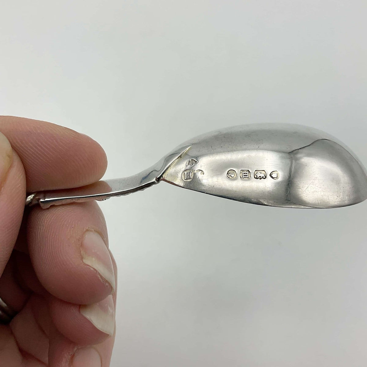 Hallmarks on the side of the tea caddy spoon held in a hand with a white background.