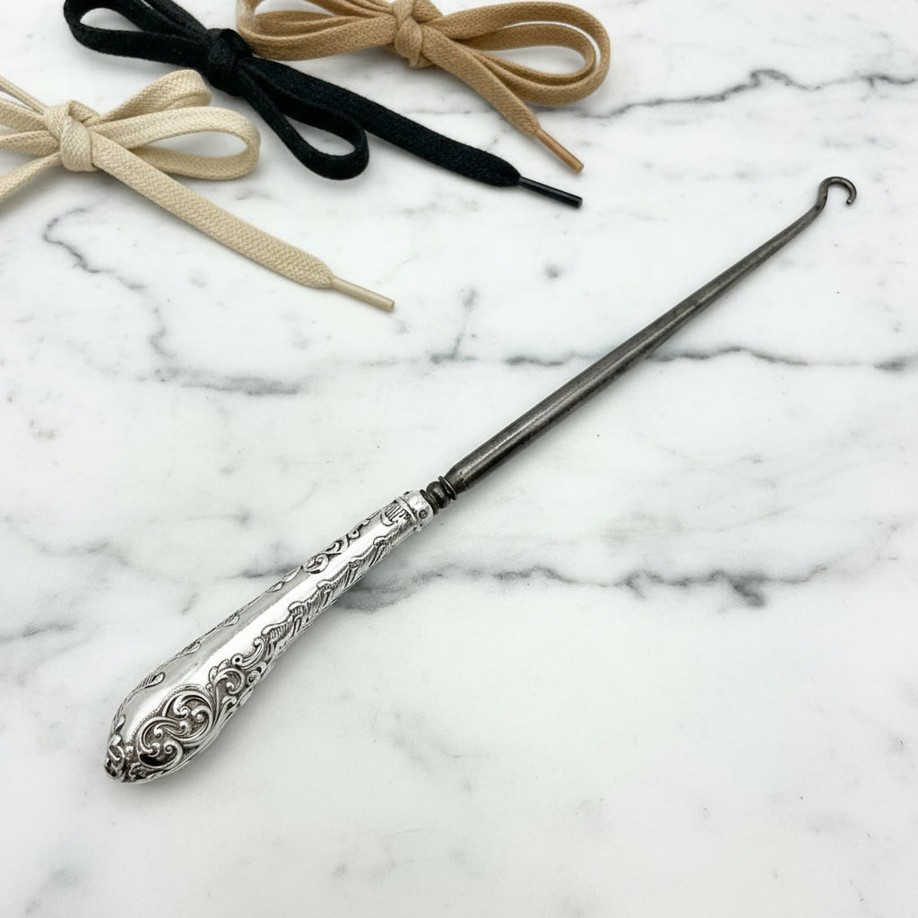 Silver handled antique button hook on a marble background with shoe laces in background