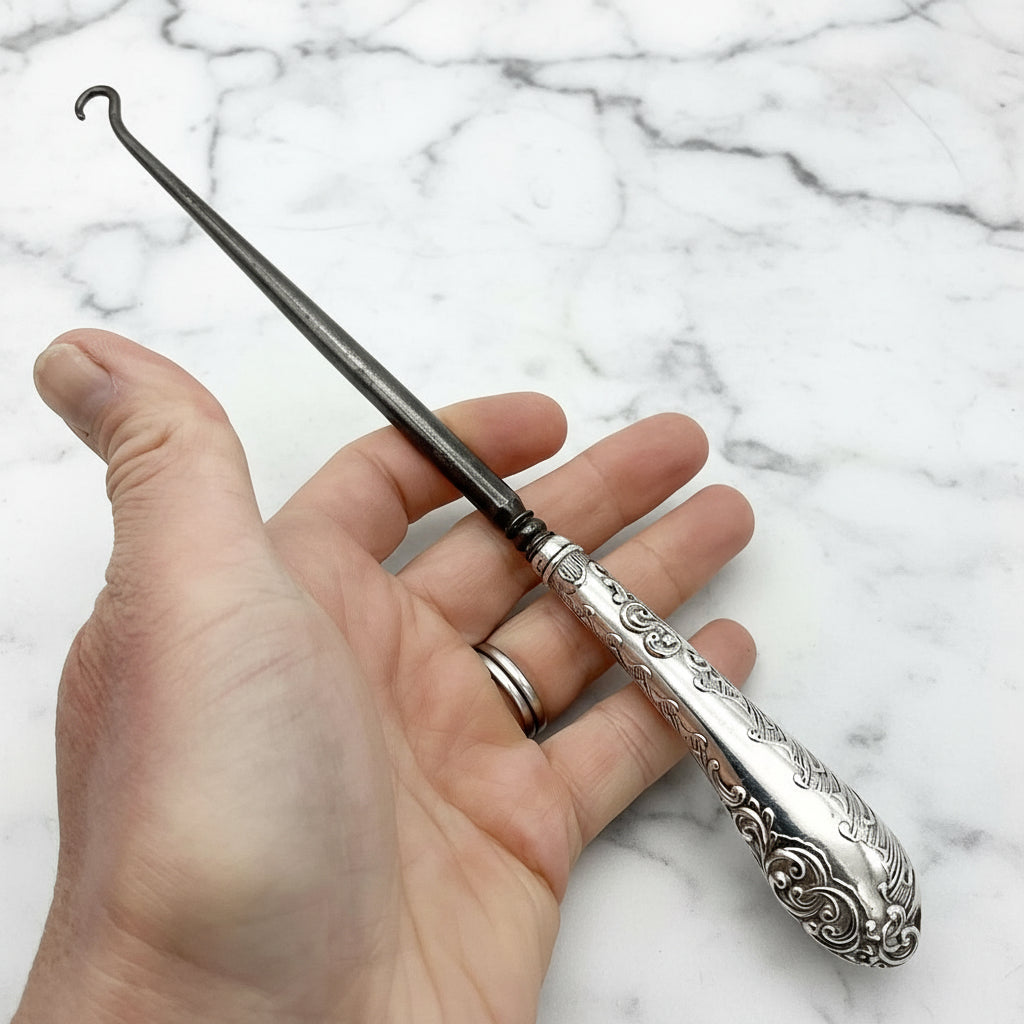 silver handled antique button hook being held in a hand with a marble background