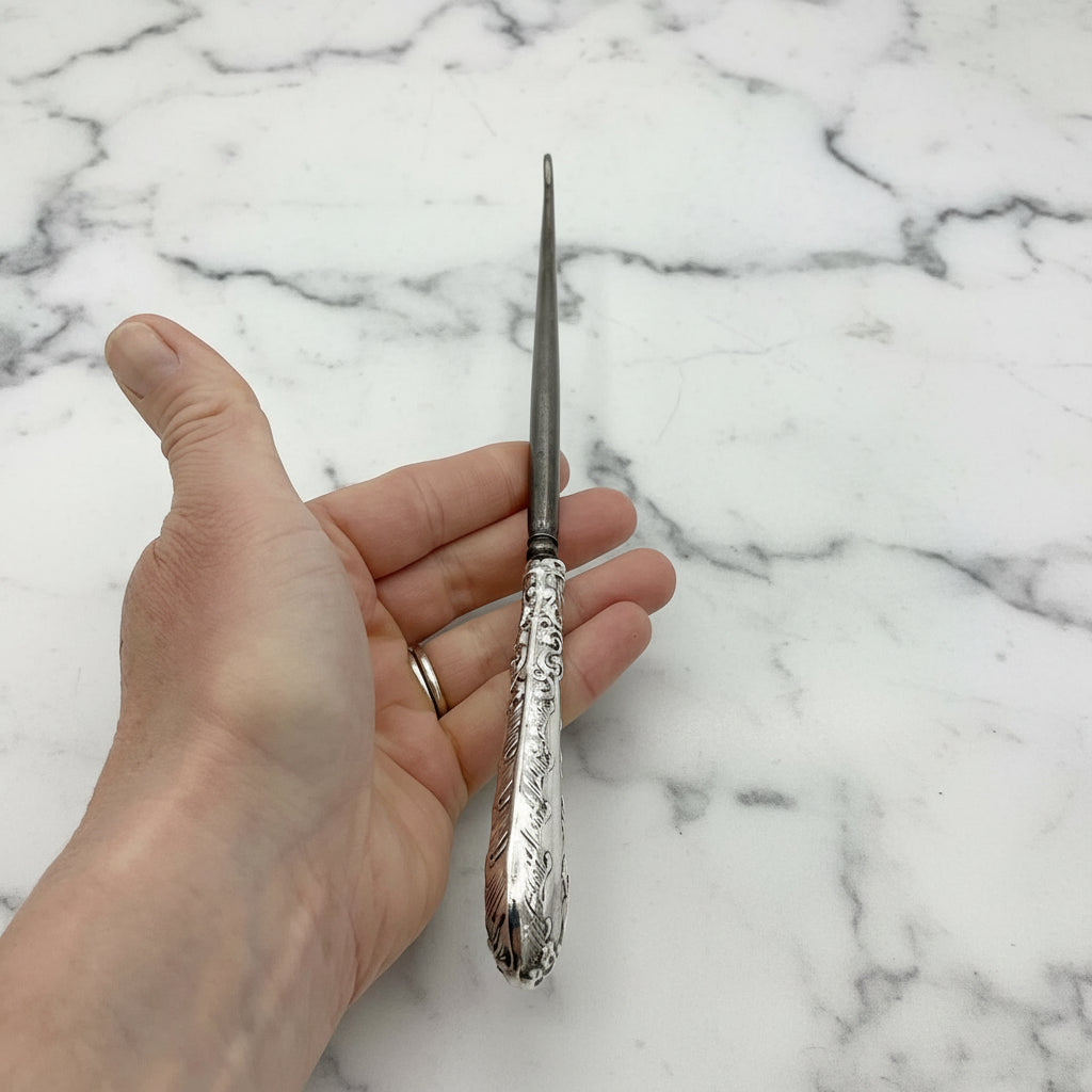 top view of silver handled antique button hook being held in a hand