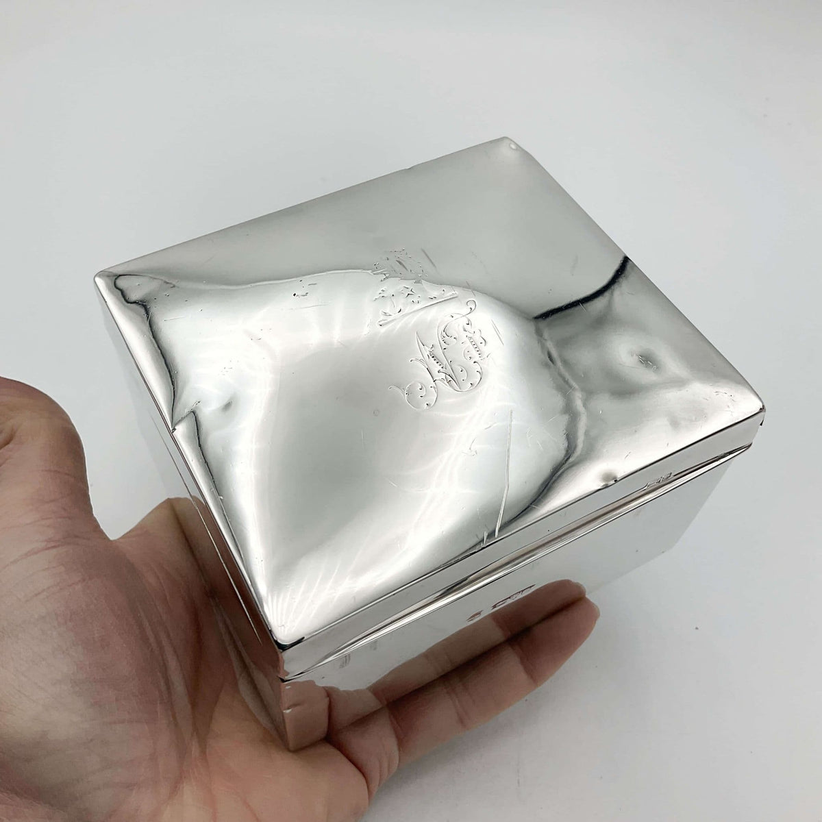 Antique Square silver cigarette box with a engraved lid held in a hand