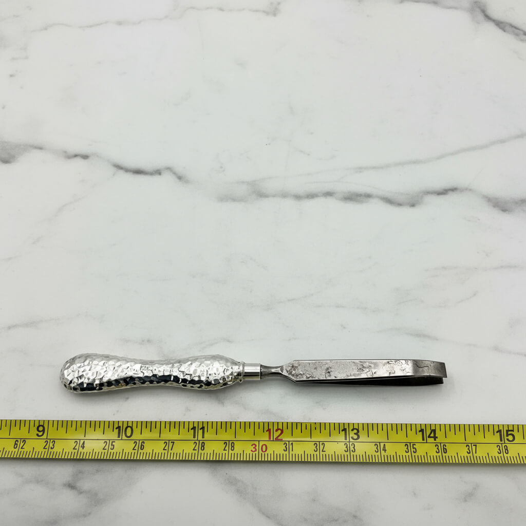 Metal tweezers with textured handle on a marble surface with a tape measure for scale.