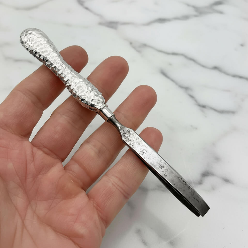 Hand holding a silver tweezers with textured handle against a marble background