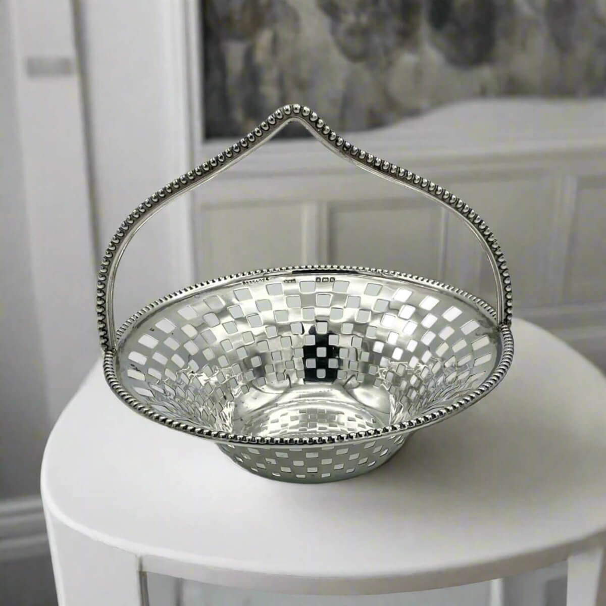 Silver decorative basket with a checkered pattern on a white surface.