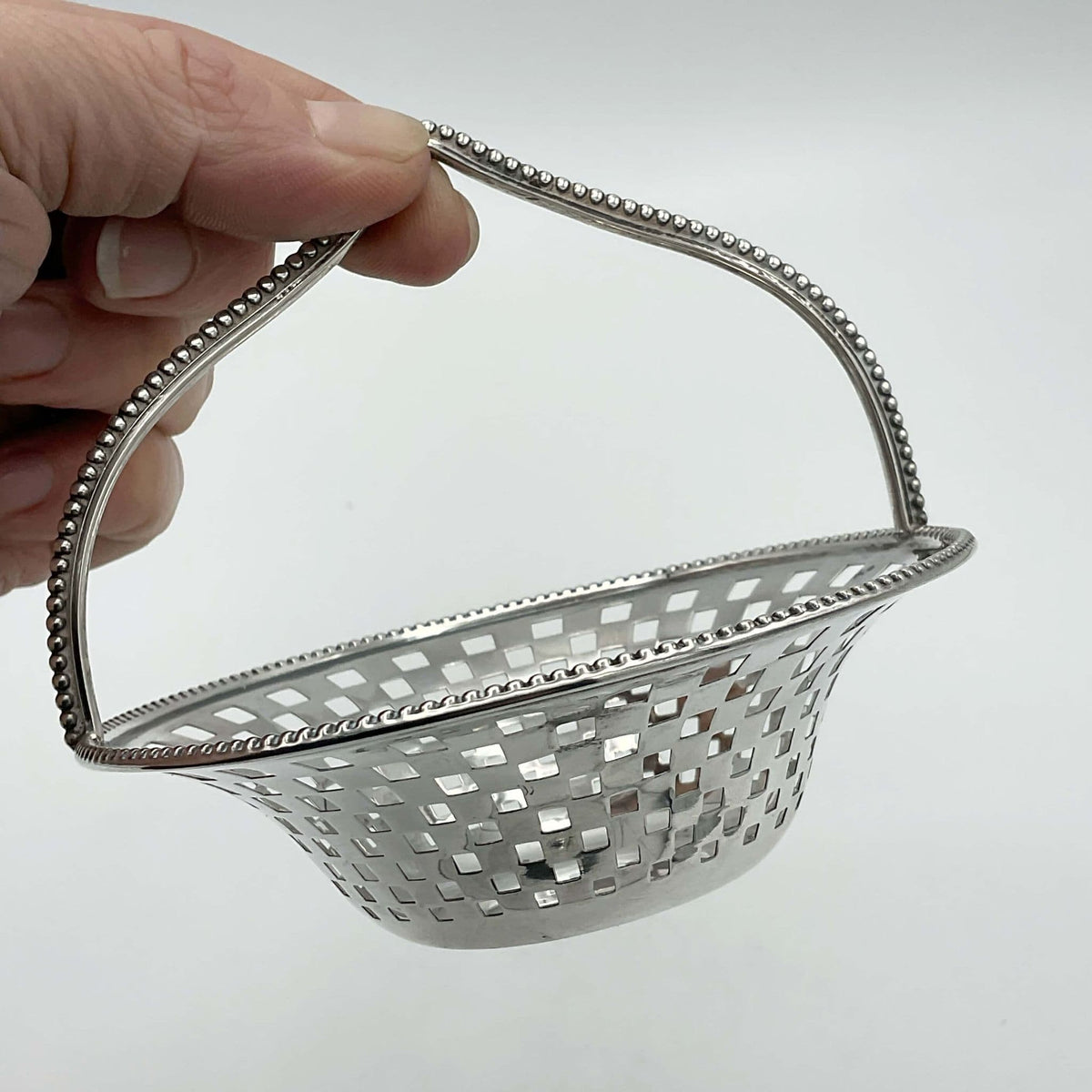 silver decorative basket held by a hand on a light gray background