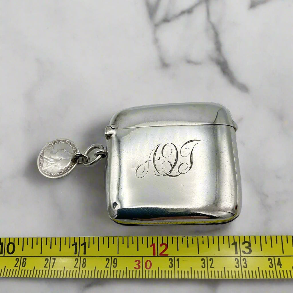 Silver vesta case with 'AQT' engraving on a marble surface with a measuring tape for scale.