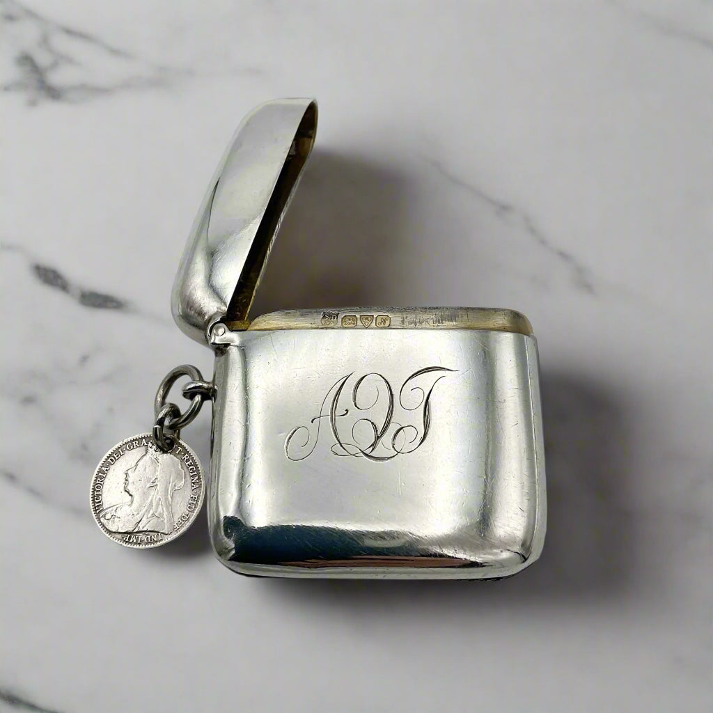 Silver vesta with hinged lid and engraved initials on a marble surface