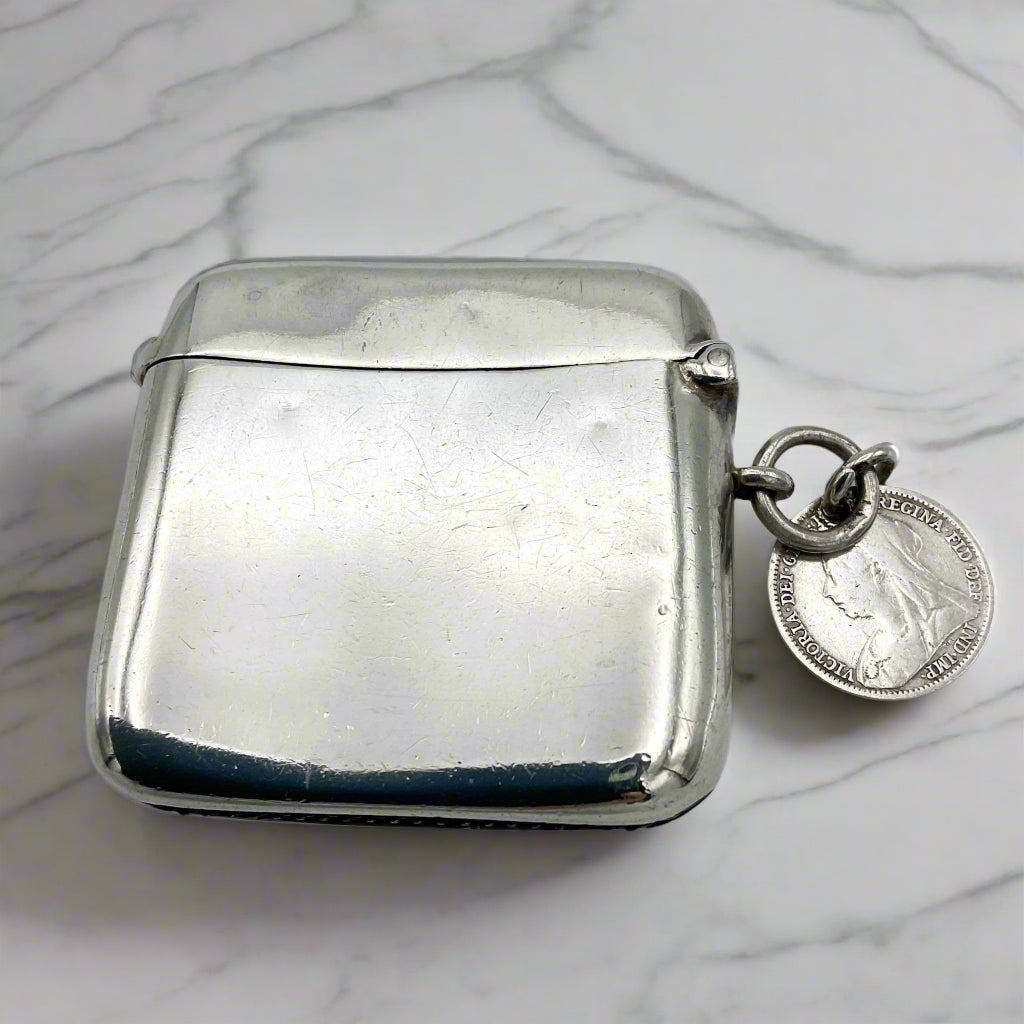 Silver vesta case with a coin attached on a marble surface